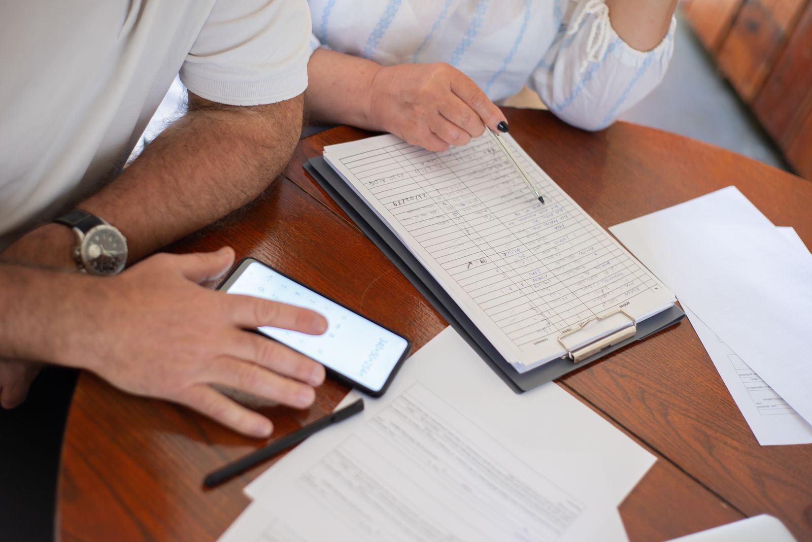 Dos personas revisan una planilla manuscrita y papeles sobre una mesa